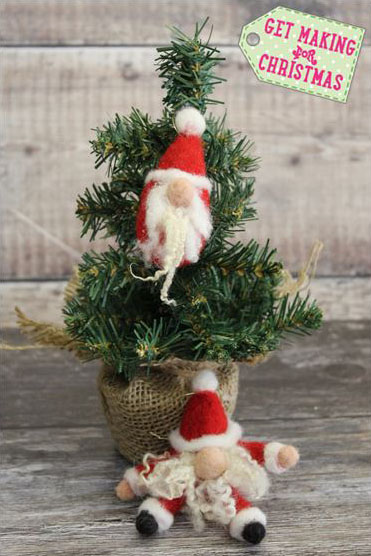 Two red and white needle felted Santas perched on a mini-Christmas tree