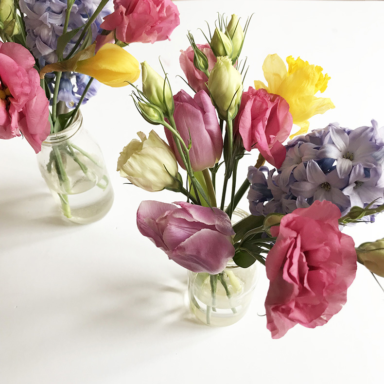 Two posies of pink, purple and yellow flowers in glass vases on a white table