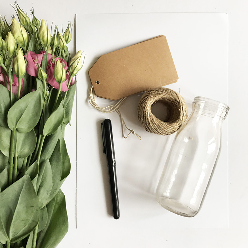 A bunch of tulips some brown paper gift tags, a pen and a vase laid out on a white surface